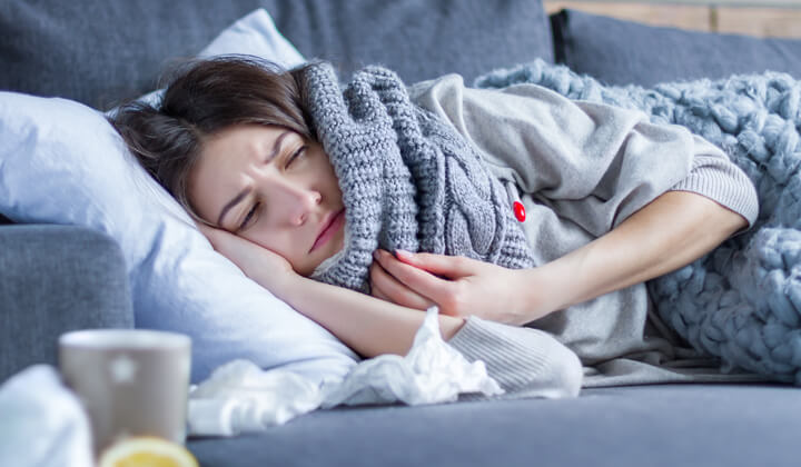 Frau mit Schal im Bett Halsschmerzen als Erkältungssymptom