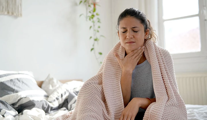 Frau mit Erkältung und Halsschmerzen Frau mit Schmerzen fasst sich an den Hals